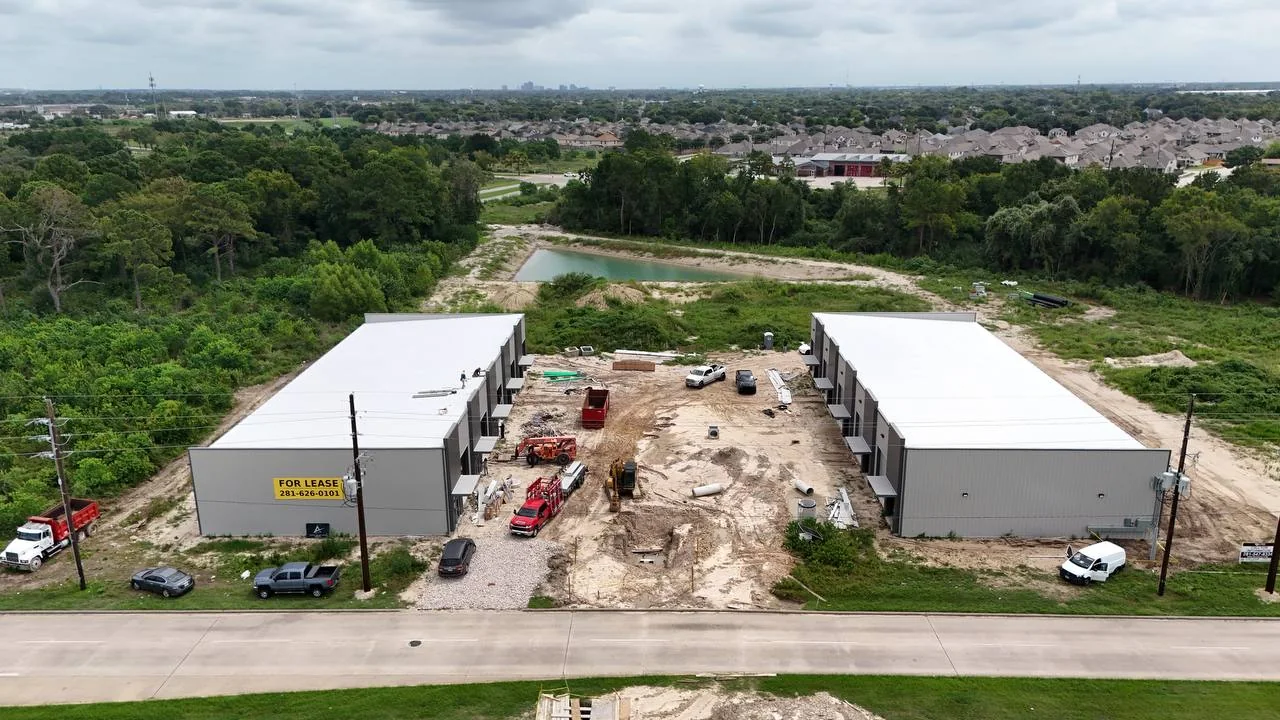 Aerial view of both Bammel metal buildings fully sheeted with roof and wall panels installed, storm pipe and structures staged in the unpaved central yard