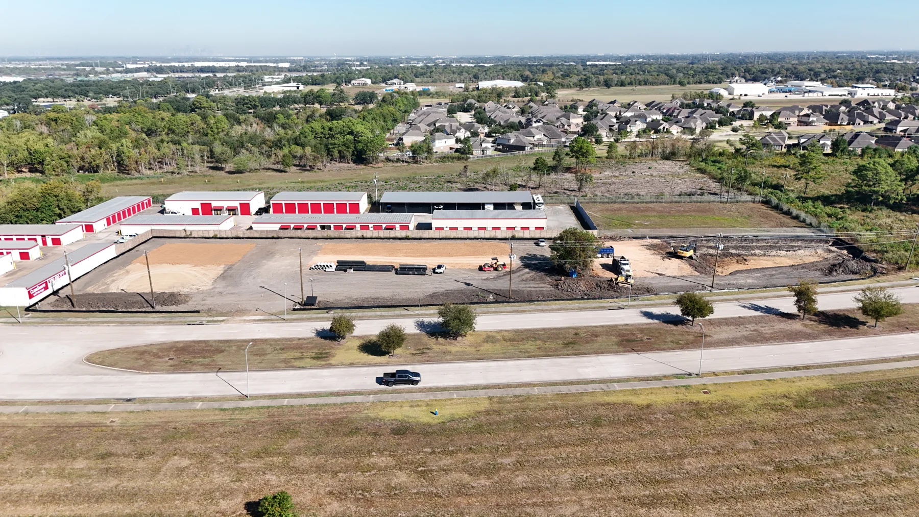 McHard Flex aerial: graded site, staged drainage pipes and excavation beside the neighboring storage facility